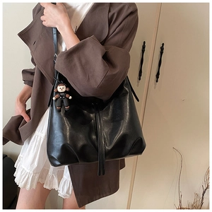 Detail of black leather tote bag with drawstring design and cute plush doll charm