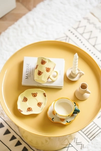 Close-up of yellow ceramic coffee mug and saucer set with cute hand-painted bear pattern
