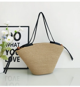 Detailed shot of beige woven tote bag featuring black shoulder straps and wooden beads