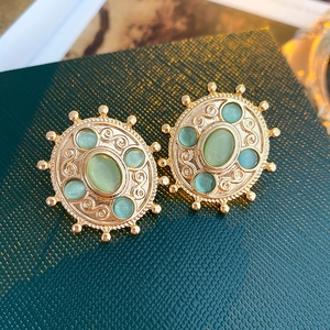 Detailed close-up of vintage gold floral earrings with green gemstones on textured surface