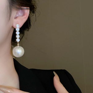 Close-up of model wearing gold tassel earrings with vertical diamonds and white pearls