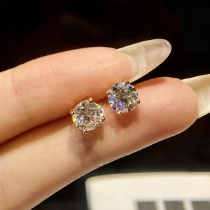 Classic moissanite stud earrings in rose gold four-prong setting held between fingers
