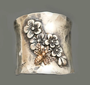 Detailed macro view of vintage silver wide band ring with embossed flowers and golden bee