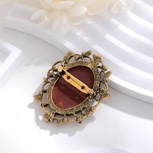 Vintage bronze brooch with brown oval gemstone and intricate filigree design on white base