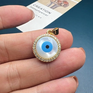 Close-up of golden evil eye shell pendant with sparkling zircons held in hand