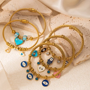Gold cable wire bracelet set with enamel evil eye hamsa and heart charms on silk background