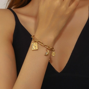 Gros plan d'un bracelet à maillons dorés avec breloques étoile et lune porté au poignet
