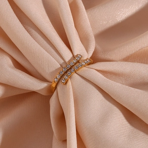 Detail of gold-plated double-layer crossover ring with clear zircons on peach silk fabric