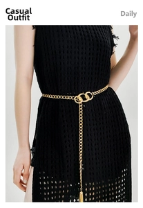 Detail of a golden metal waist chain with double ring buckle and tassel on black dress