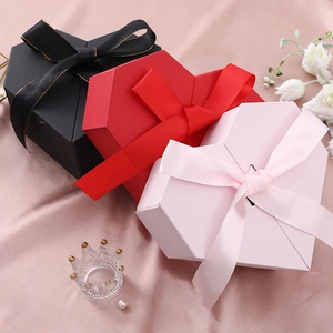 Three heart-shaped gift boxes in red, black and pink with satin ribbons on silk fabric