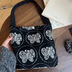 Retro canvas underarm bag with butterfly embroidery and silver snap button on wood background