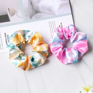 Detailed view of colorful tie-dye satin scrunchies on a white marble background