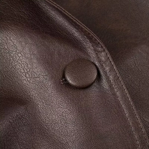 Macro shot of dark brown leather jacket featuring a round covered button and premium stitching