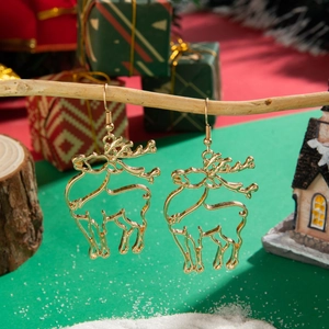Détail de boucles d'oreilles renne dorées ajourées sur un décor de Noël enneigé