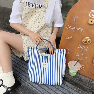 Close-up of blue and white striped canvas tote bag with woven brand label on a wooden stair