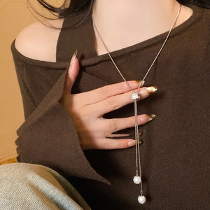 Détail d'un collier Y en perles argentées avec curseur zircon sur maille marron