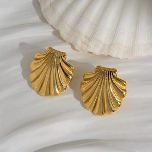Golden seashell stud earrings with textured surface resting on elegant white silk fabric