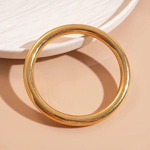 Bracelet jonc en acrylique doré poli au design géométrique circulaire sur une assiette décorative