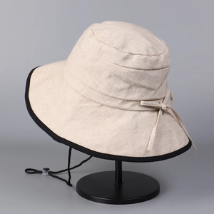 Close-up of beige cotton linen sun hat featuring black trim, bow detail and wind cord