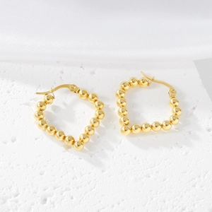 Detail of high-polish gold beaded heart-shaped earrings on elegant white silk background