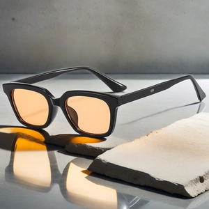 Detail of square black frame sunglasses with orange lenses and silver rivets on a stone