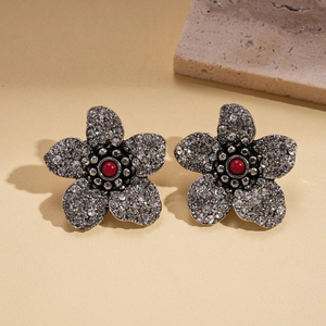 Detail von dunklen Blumenohrringen mit Silberfinish, weißen Kristallen und roter Perle