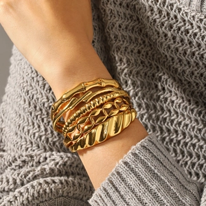 Close-up of stacked gold titanium steel bracelets featuring various textures on wrist