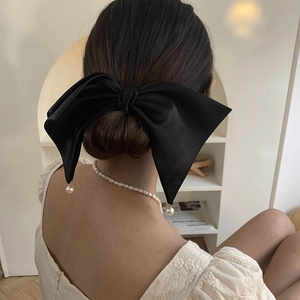 Detail of a black satin bow hair clip featuring elegant white pearl pendant charms