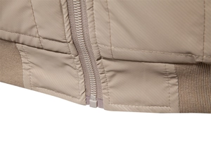 Macro detail of khaki jacket showing resin zipper, quilted stitching, and ribbed hem