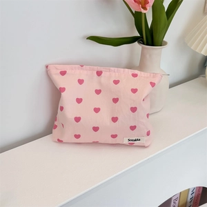 Detail of pink canvas pouch with red heart patterns and woven brand label on white surface