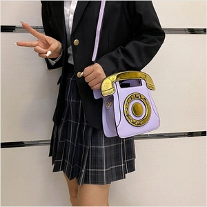 Model wearing a purple retro telephone shaped crossbody bag with gold dial detail