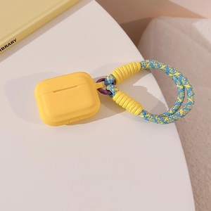Detail of yellow silicone AirPods case with blue and yellow braided lanyard on a desk