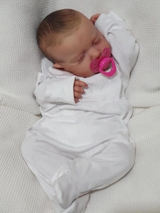 Close-up of sleeping 19-inch reborn doll with pink pacifier and white smocked outfit