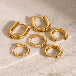 Three pairs of gold stainless steel hoop earrings with cubic zirconia stones on stone surface