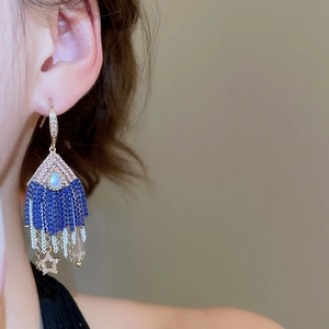 Detail of blue bead earrings with gold star tassels worn by a model in soft light