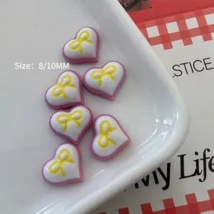 Macro detail of heart-shaped resin nail charms with pink border and yellow bow pattern