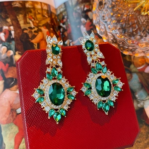 Macro shot of vintage gold emerald earrings with oval stones and crystal detailing