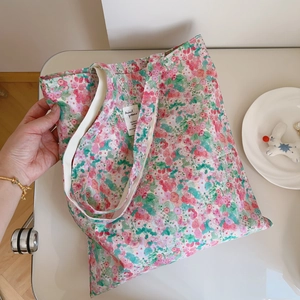 Detailed top view of a pink floral cotton tote bag with a woven brand tag on the surface
