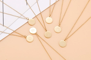 Détail de pendentifs ronds dorés avec lettres majuscules gravées sur une chaîne maille