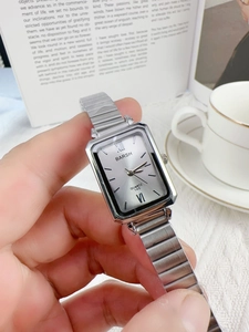 Close-up of silver square quartz watch with metal link strap and roman numerals on dial