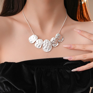Detail of silver hammered irregular oval pendants on a snake chain worn on model