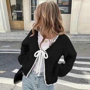 Detail showing oversized white bow tie and wavy lace trim on black knitted cardigan