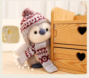Close-up of cute plush penguin wearing a red knitted hat and scarf on a wooden desk