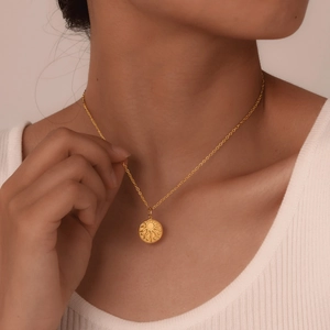 Close-up of a vintage golden sunburst pendant necklace worn by a female model on a white shirt