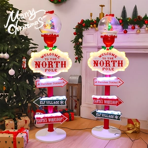 Lighted North Pole sign post with Christmas tree globe near a warm fireplace