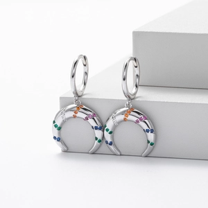 Macro shot of silver crescent moon earrings with colorful zircon stones on white steps