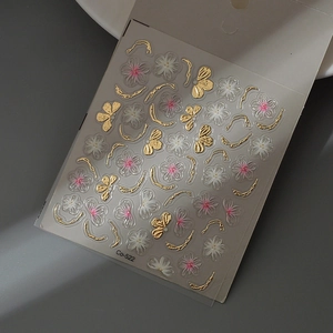 Dettaglio di adesivi 3D per unghie con farfalle dorate e fiori bianchi in rilievo