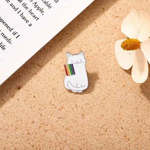 Detail of a white cartoon cat enamel pin holding a rainbow flag on cork board