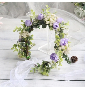 Detail view of artificial flower crown with purple roses, green leaves and white ribbons