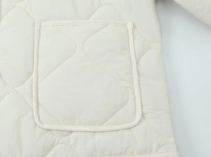 Macro detail of diamond quilted stitching and reinforced pocket edge on cream jacket
